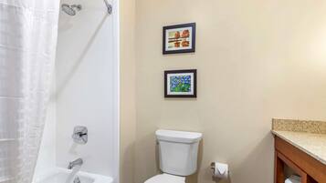 A bathroom with a white bathtub, a toilet, and two framed pictures on the wall.