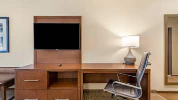 Camera d'albergo con una scrivania in legno, una TV a schermo piatto, una lampada e una sedia.