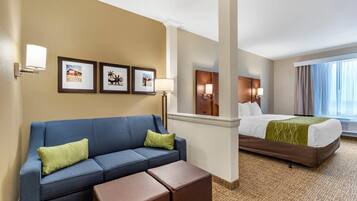 Une chambre d’hôtel avec un canapé bleu, un lit recouvert d’une couverture verte et des tableaux encadrés accrochés au mur.