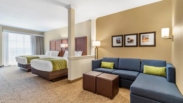 A hotel room with two beds, a blue sofa, a coffee table, and framed pictures on the wall. - Comfort Suites San Antonio Ft. Sam Houston/SAMMC Area (San Antonio)