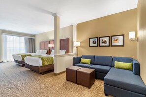 A hotel room with two beds, a blue sofa, a coffee table, and framed pictures on the wall.