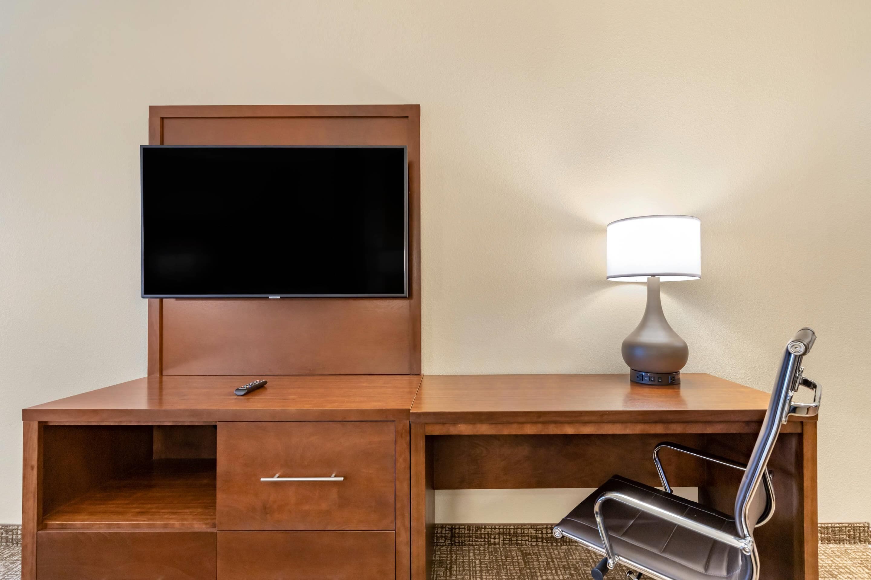 A wooden desk with a flat-screen TV, a lamp, and a chair.