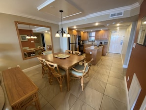 A spacious dining area with a wooden table and chairs, a kitchen in the background, and a large mirror on the wall.