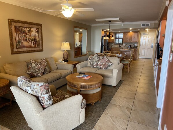 A spacious living room with a ceiling fan, a dining area with wooden furniture, and a kitchen with modern appliances.