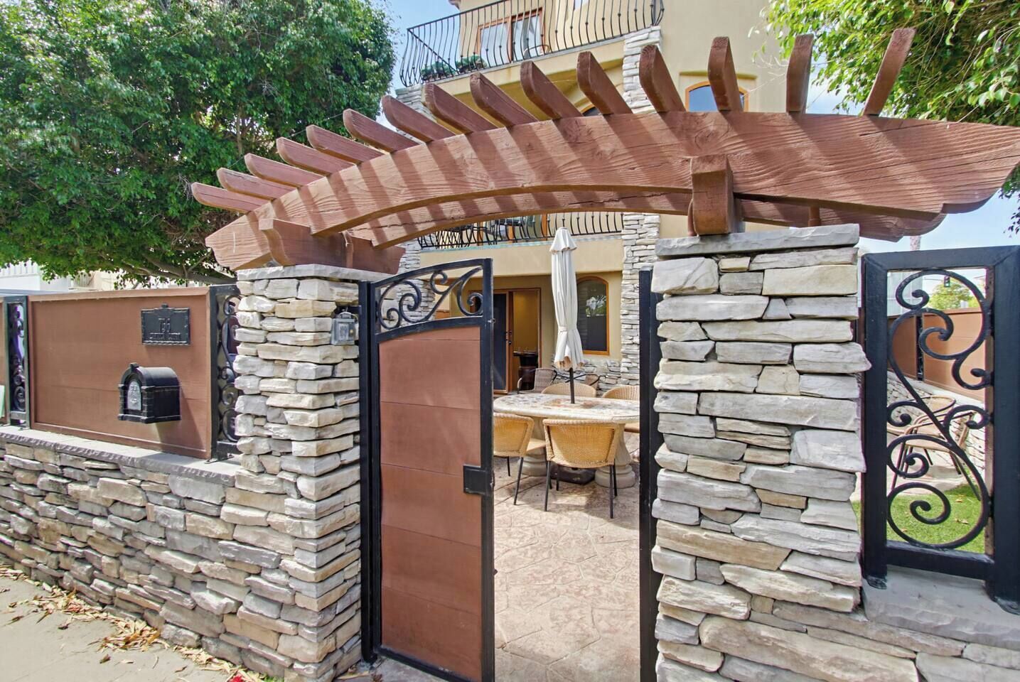 A gated entrance with a pergola, stone walls, and a mailbox.