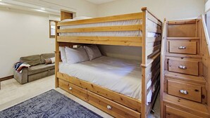 A bunk bed with storage drawers, a sofa, and a patterned rug in a room with white walls and a ceiling light. - New Photos! Luxury Steps to Beach w/hot tub garage (San Diego)