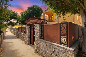 A residential area with stone walls, a gated entrance, and a pathway leading to a building with a balcony.