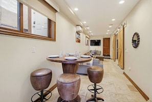 A dining area with a round table, two stools, and a television in the background.