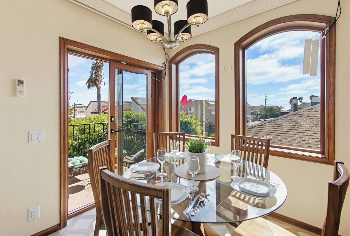 A dining area with a round glass table, wooden chairs, and a ceiling light fixture.