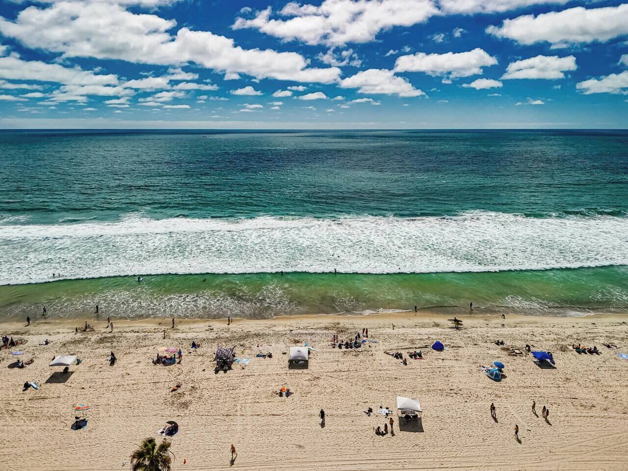 Ein Strand mit Menschen, Sonnenschirmen und blauem Himmel.