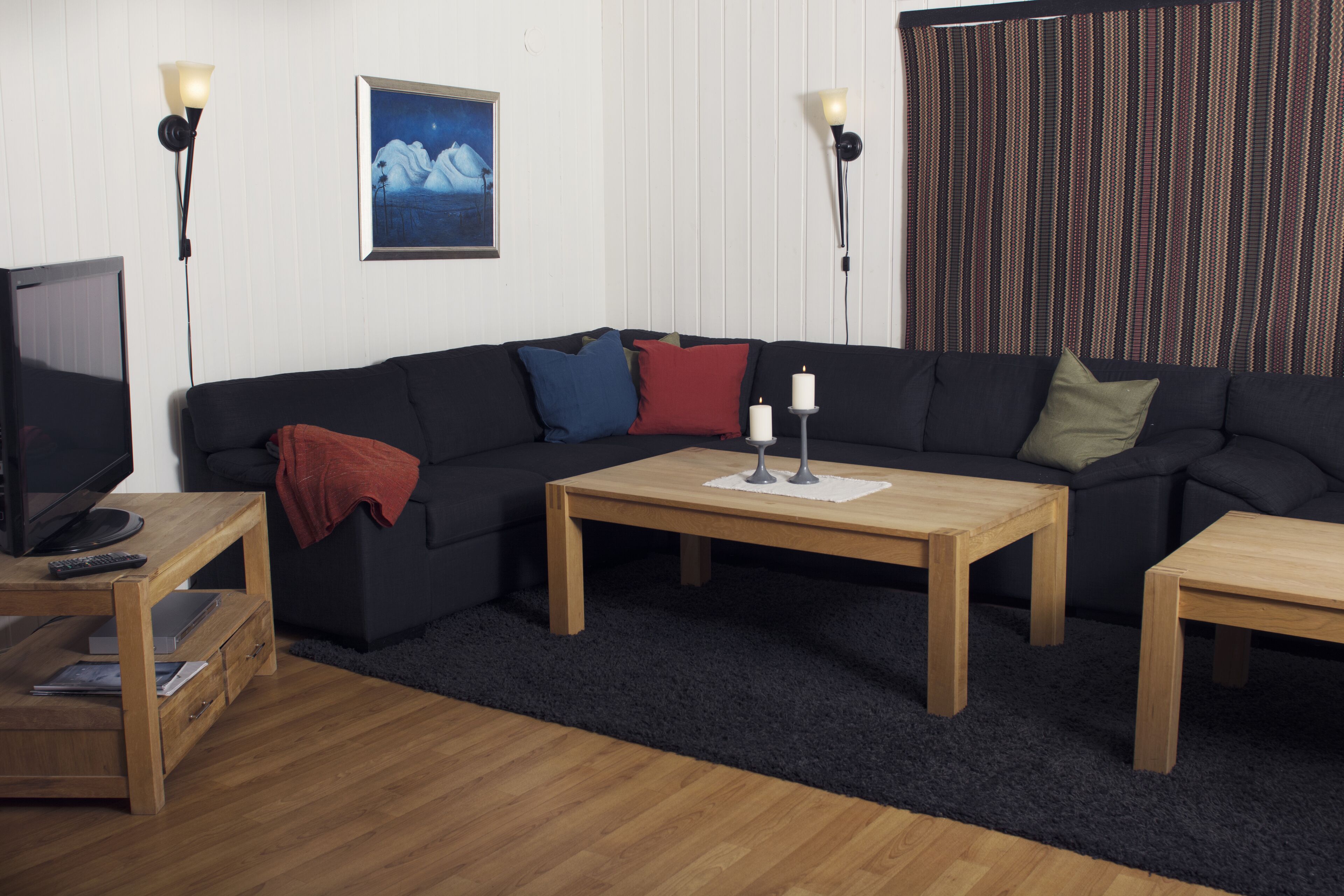 Una sala de estar con un sofá de color oscuro, dos mesas de centro de madera, un televisor sobre un mueble de madera y un cuadro enmarcado en la pared.
