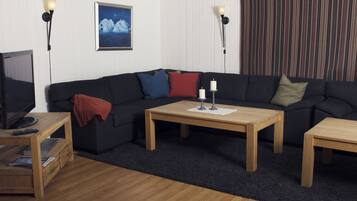 Una sala de estar con un sofá de color oscuro, dos mesas de centro de madera, un televisor sobre un mueble de madera y un cuadro enmarcado en la pared.