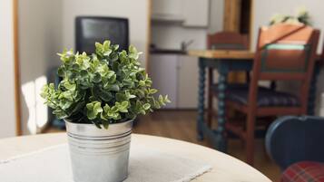 Ein Blumentopf auf einem runden Tisch in einem Raum mit Holzboden, einem Stuhl und einem Fernseher im Hintergrund.