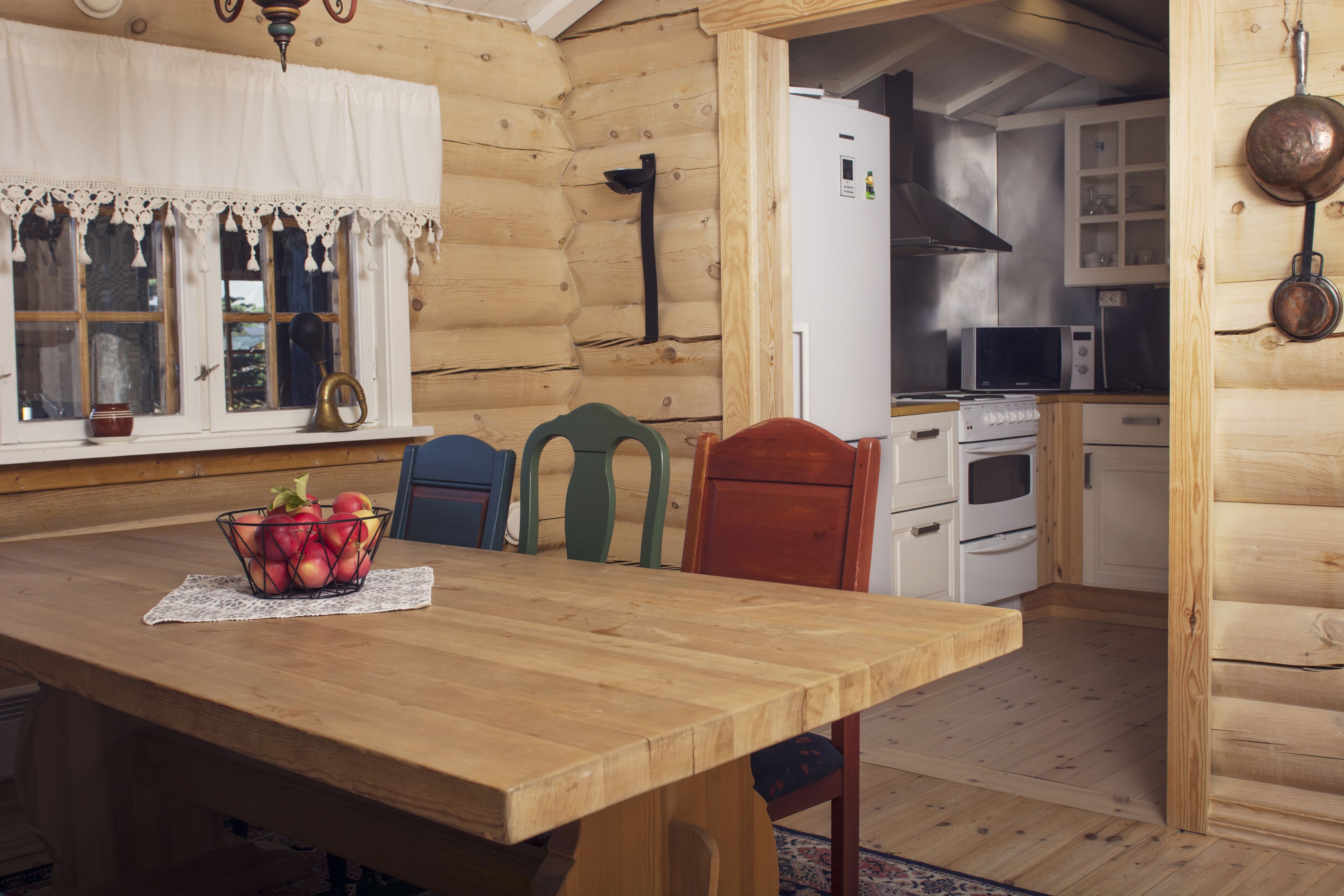 A wooden interior with a dining table, chairs, a refrigerator, and a microwave.