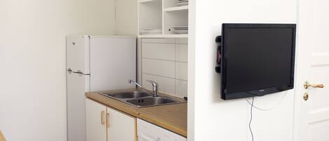 Una cocina compacta con armarios blancos, encimera de madera, pileta de acero inoxidable y televisor negro montado en la pared.