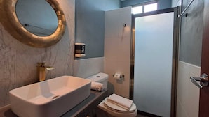 A modern bathroom with a large oval mirror, a rectangular sink, a toilet, and a shower area. - Maria-Maria Hotel (Bacalar)
