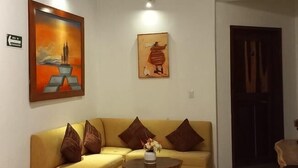 A living room with a yellow sofa, a round coffee table, and two paintings on the wall. - Maria-Maria Hotel (Bacalar)