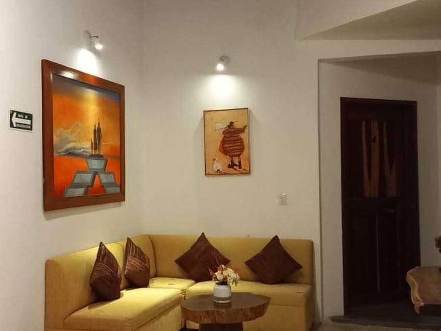 Un salón con un sofá amarillo, una mesa de centro redonda y dos cuadros en la pared.