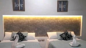 Two twin beds with matching headboards, each adorned with a swan decoration and a pillow. The room features a textured wall with 'love' and 'live' framed on the upper part. - Maria-Maria Hotel (Bacalar)