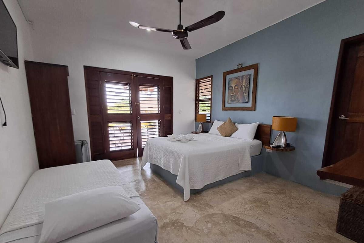A room with two beds, a ceiling fan, and a window with shutters.