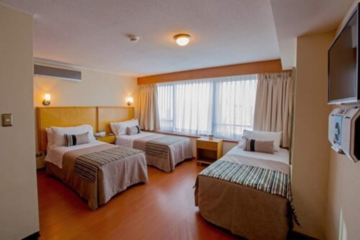 Ein Hotelzimmer mit zwei Einzelbetten, einem großen Fenster mit Vorhängen, einem Flachbildfernseher und einem Nachttisch.