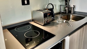 A modern kitchen with a built-in induction cooktop, a toaster, a kettle, and a stainless steel sink. - RQ Express Costanera (Santiago)