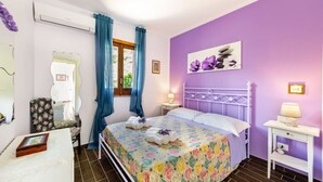 Un dormitorio con cama, una silla, una mesita de noche, una lámpara y una ventana con cortinas.