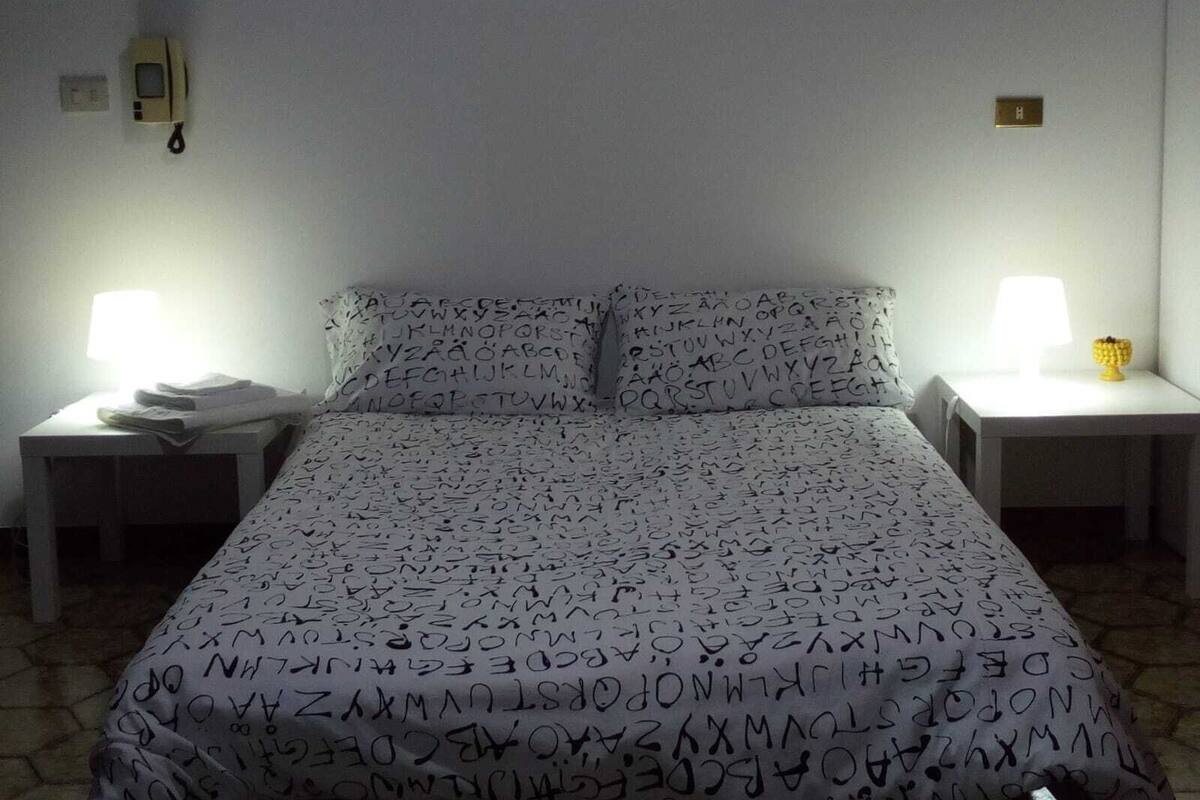 A bedroom with a bed, two bedside tables, a lamp, and a wall-mounted light fixture.