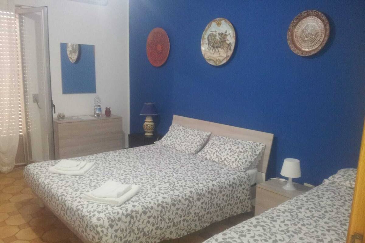 A bedroom with two beds, a nightstand, a lamp, and decorative plates on the wall.