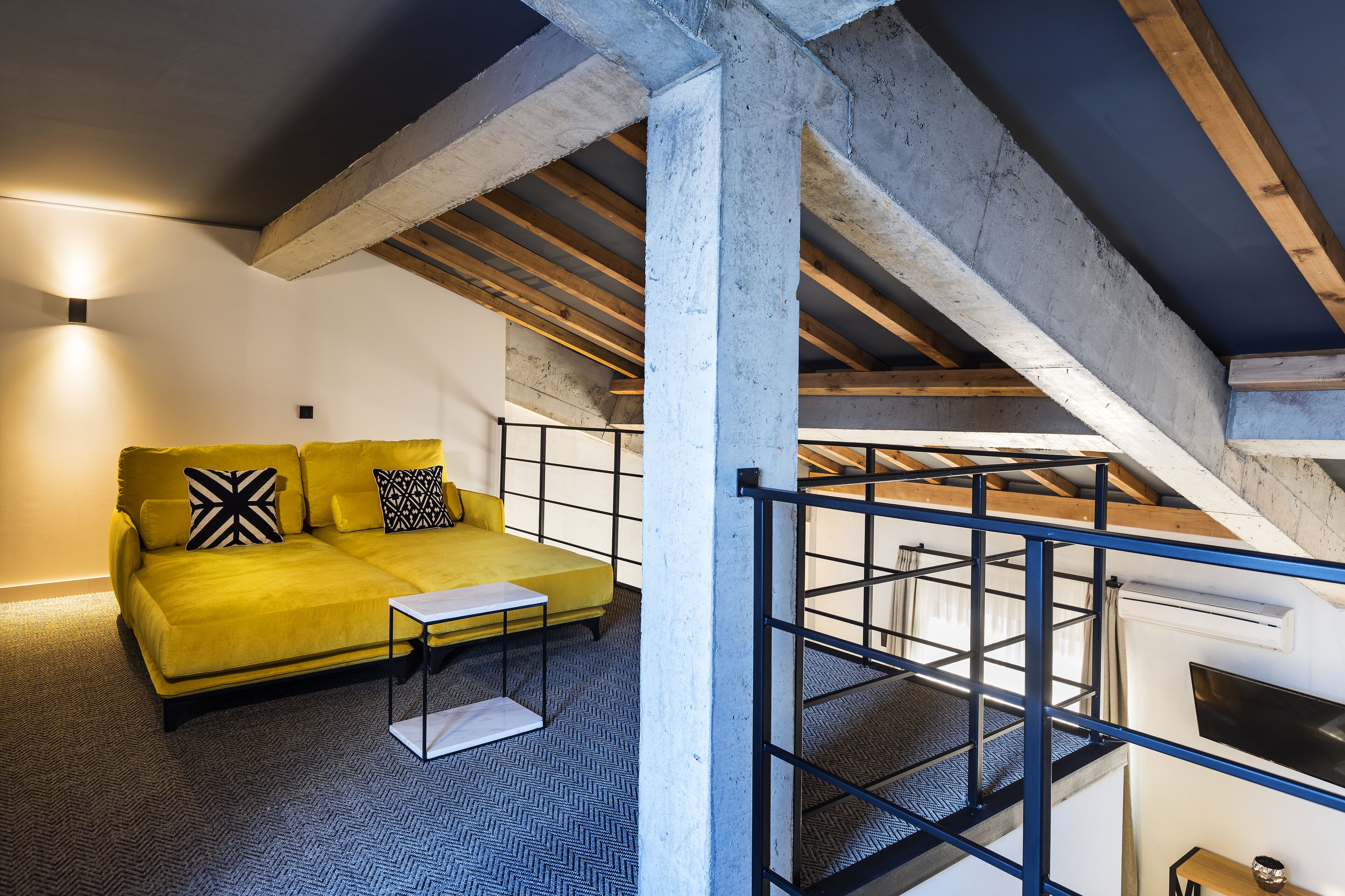 A yellow sofa with black and white pillows, a small white table, and a herringbone-patterned floor.