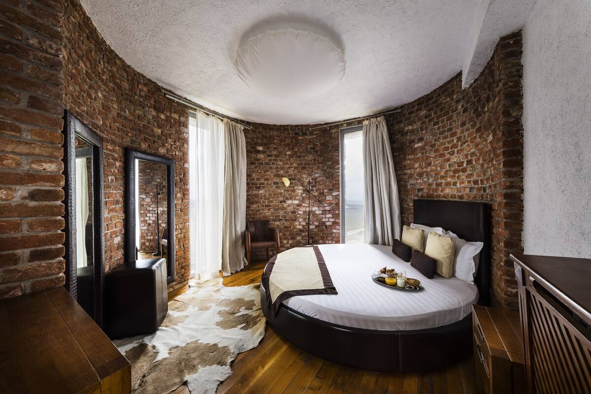A bedroom with a brick wall, a round bed, a wooden dresser, and a cowhide rug.