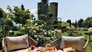 An outdoor seating area with wicker chairs and a table set with food and drinks, overlooking a garden with roses and a historic tower. - Maison & Chateau Copsa (Karlovo)