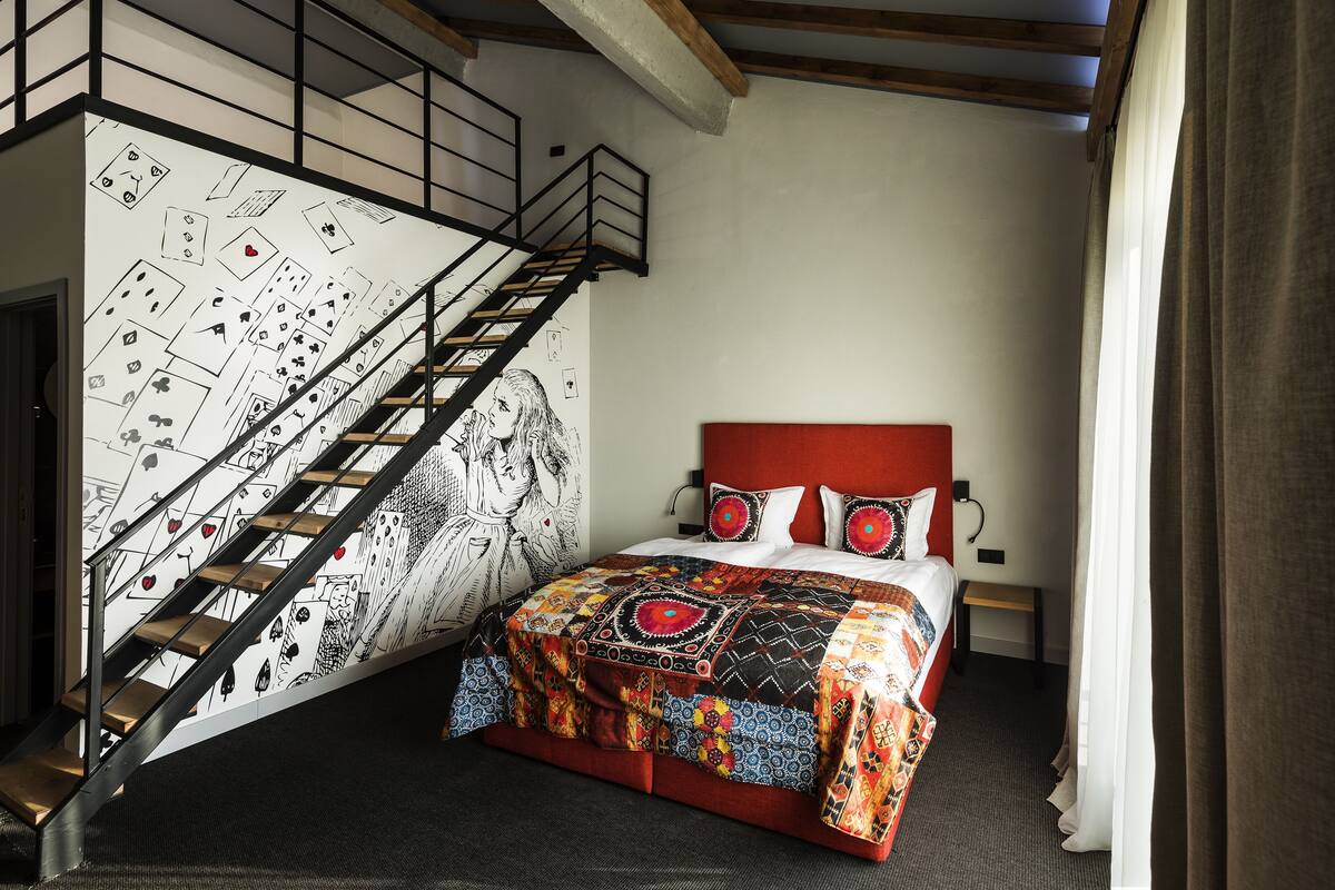 A bedroom with a bed, a staircase, and a wall with card game illustrations.