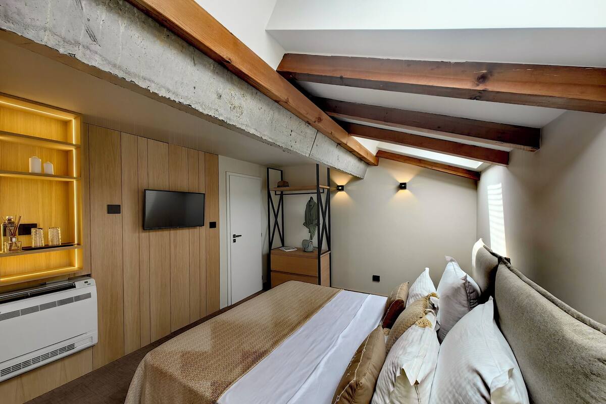 A bedroom with a bed, bedside table, wall-mounted TV, and built-in shelving with decorative items.