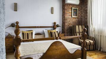 A traditional wooden bed with a headboard, a nightstand, a striped armchair, and a brick wall with a picture.