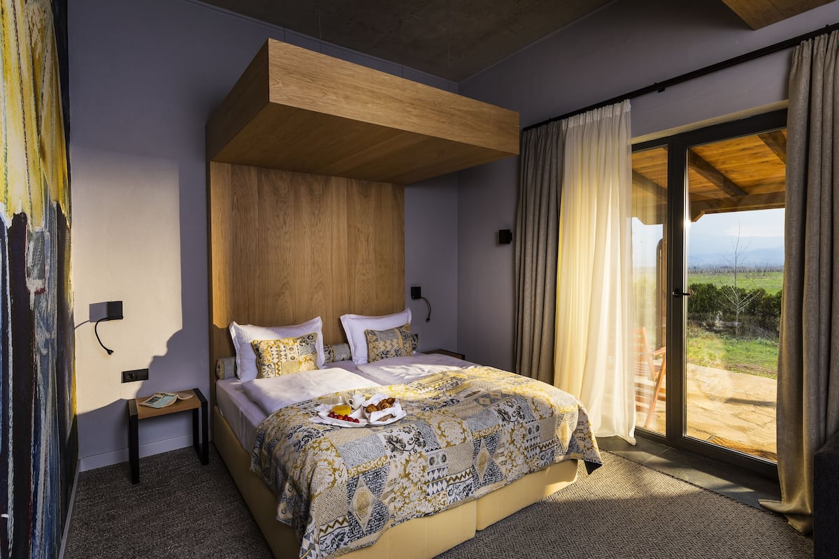 A bedroom with a large bed, a wooden headboard, a small bedside table, and a view of the outdoors through a sliding glass door.
