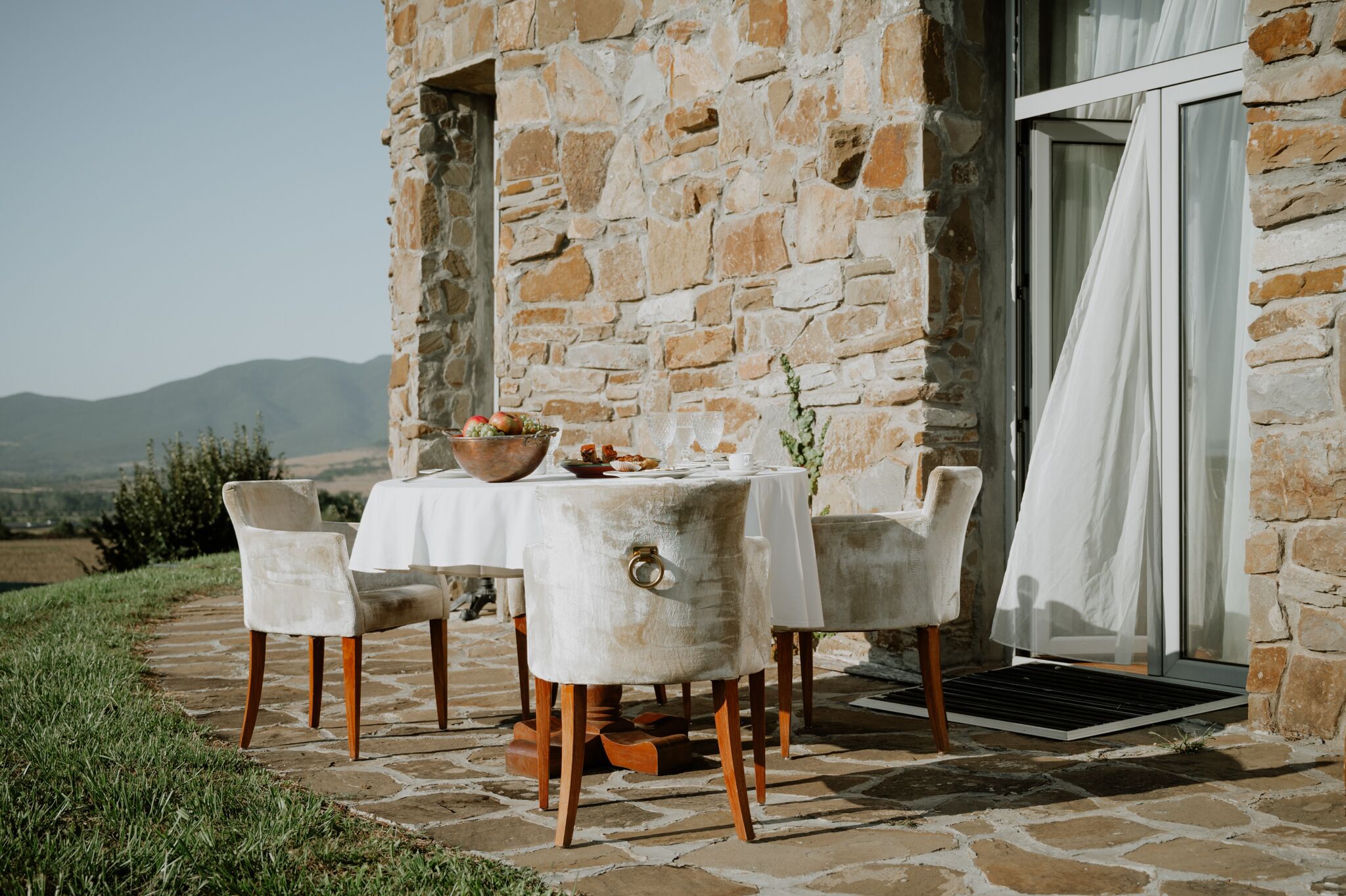 Un edificio de piedra con una mesa para dos, un frutero y vistas al campo.
