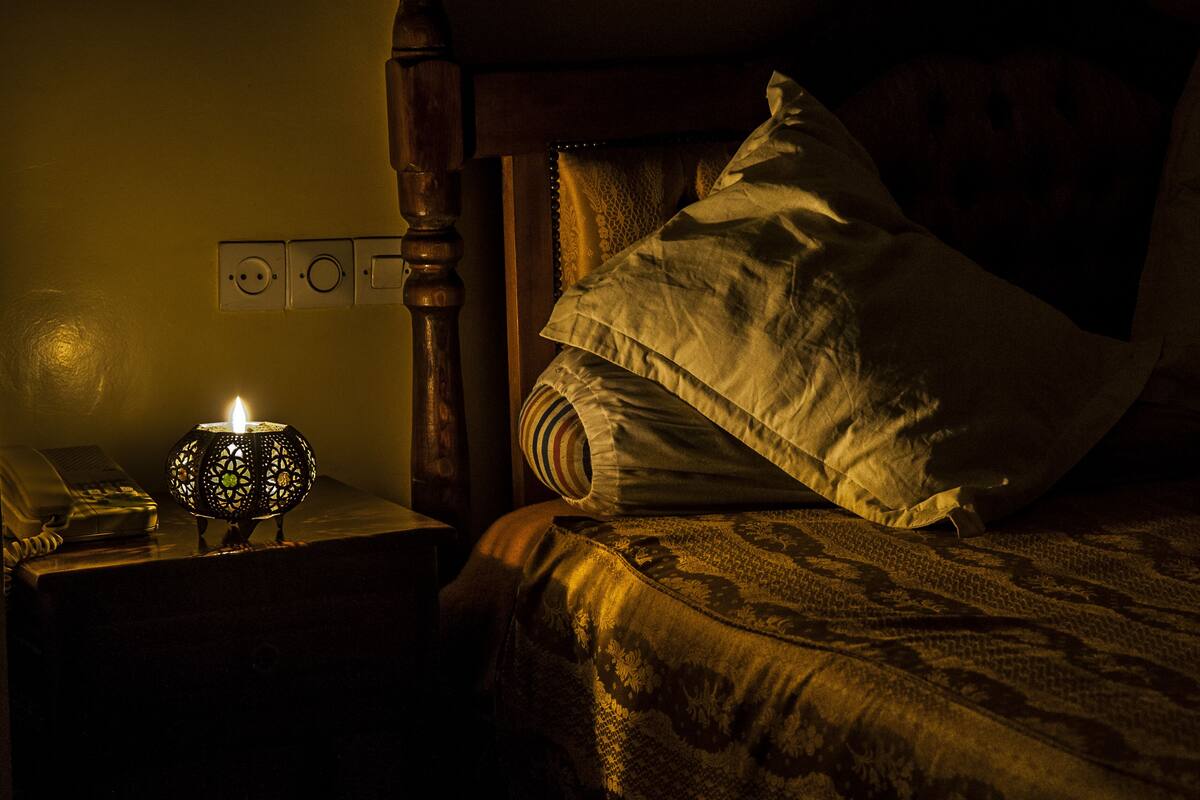 A dimly lit room with a wooden headboard, a patterned bedspread, and a nightstand with a lamp and a telephone.