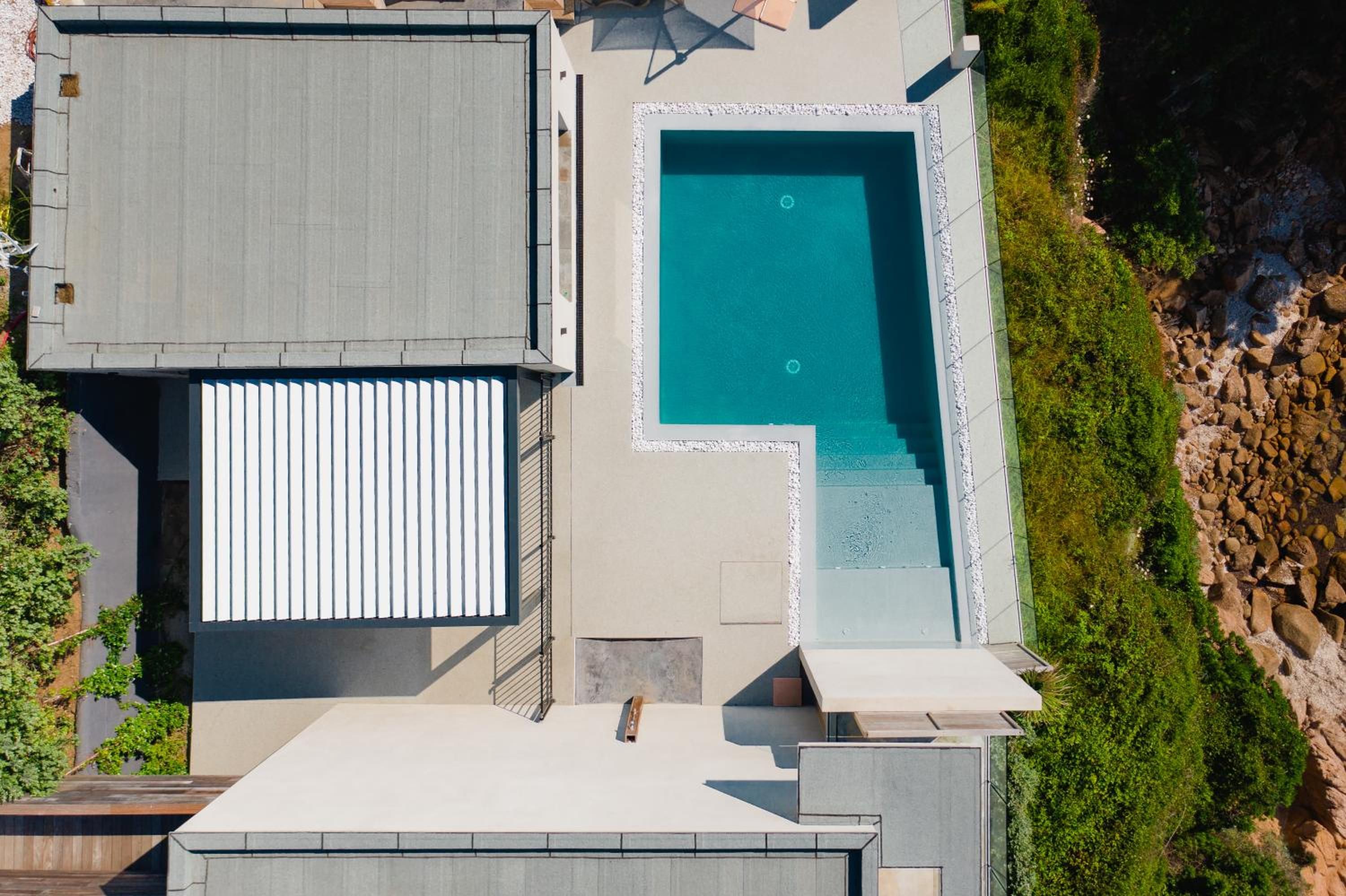 A rooftop with a swimming pool, a covered patio, and a view of a rocky coastline.