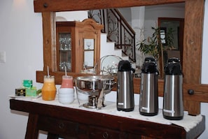 A breakfast bar with various food items and beverages, a large metal pot, and several stainless steel thermos bottles.