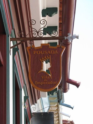 Un letrero de madera con el texto "POUSADA Vila do Imperador" colgado de una estructura metálica.