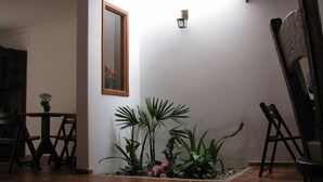 Een kamer met een betegelde vloer, een spiegel met houten lijst, een tafeltje met een bloempot en een stoel.
