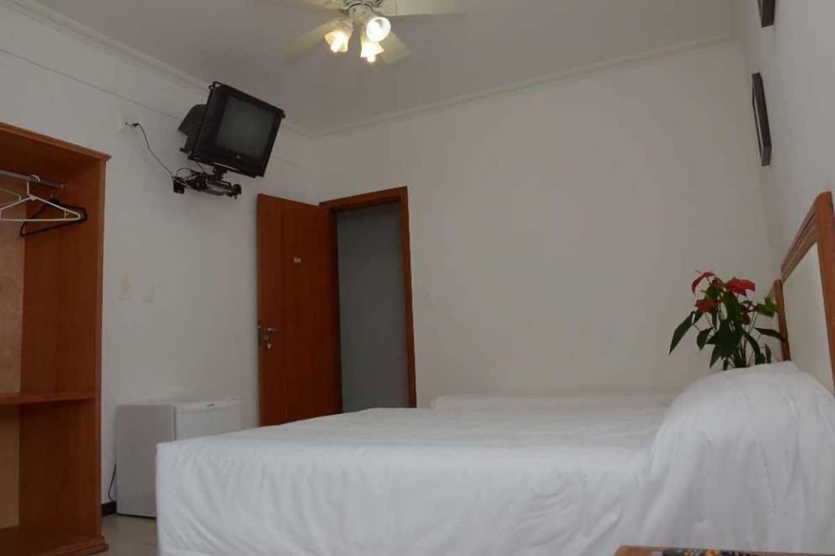 A bedroom with a bed, a television mounted on the wall, a ceiling fan, and a door.