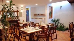 Een restaurant met houten tafels en stoelen, plantenbakken en een betegelde vloer.
