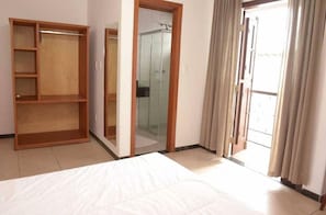 A bedroom with a bed, a wooden wardrobe, a glass shower, and a sliding glass door to the outside.