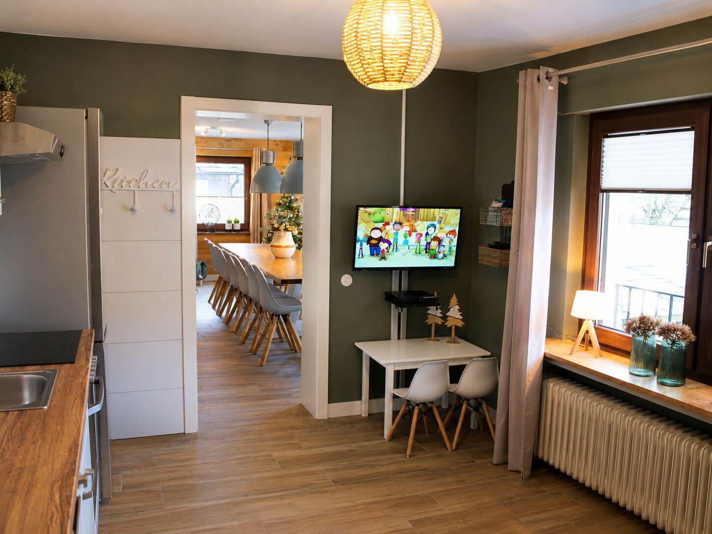 A modern kitchen with a built-in oven, a dining area with a table and chairs, a television, and a window with curtains.