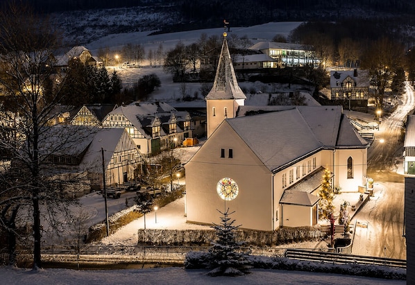 Un village enneigé, avec une église, des maisons et une montagne en arrière-plan.