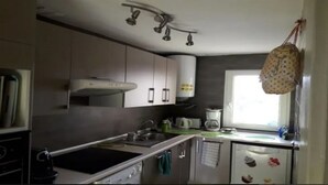 A compact kitchen with a stove, sink, and a hanging pot rack. - apartment sea view large terrace (Xàbia)