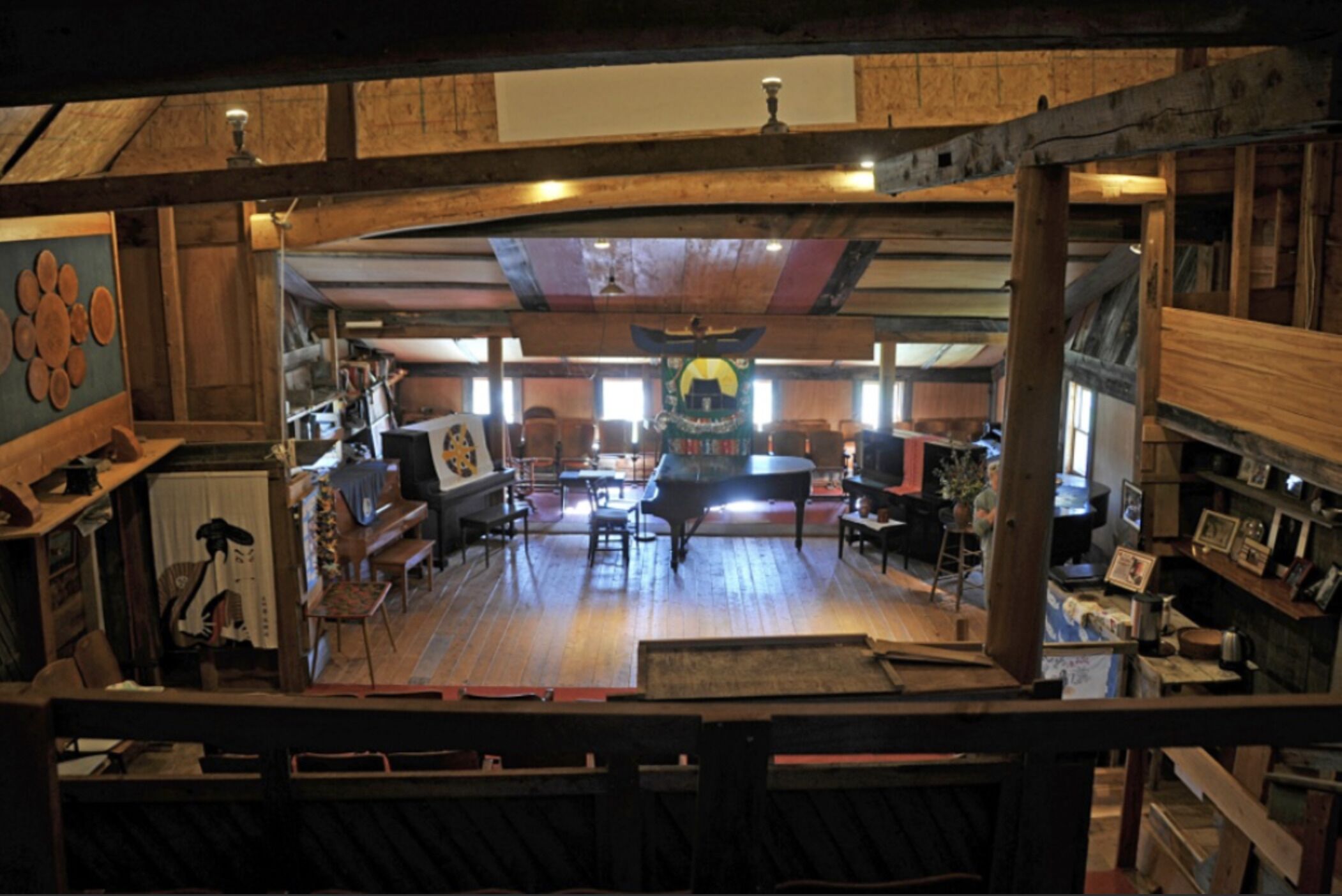 Un interior rústico con vigas de madera, un piano de cola y diversas obras de arte.