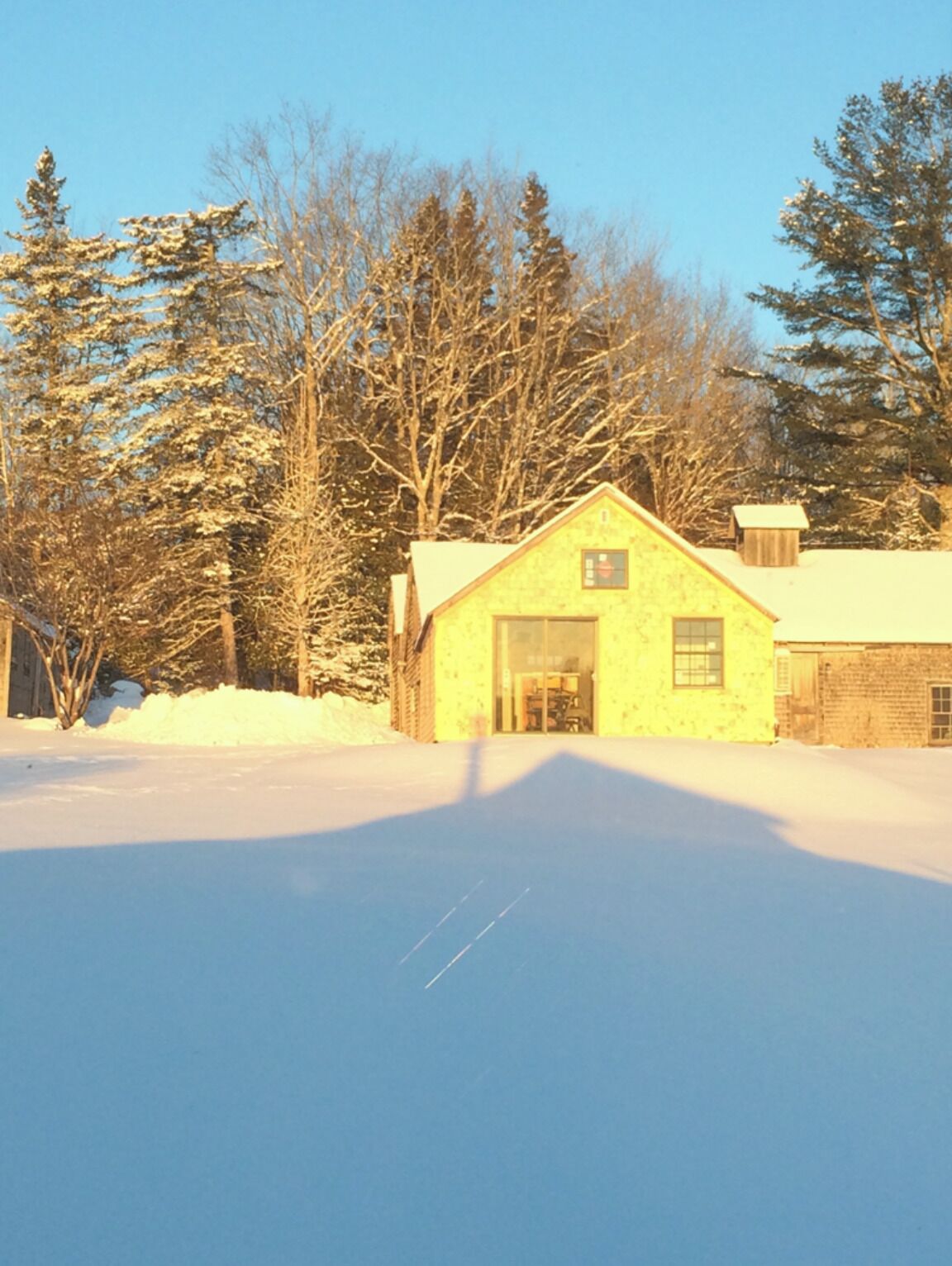 A yellow building with a large door and windows, surrounded by snow and trees.